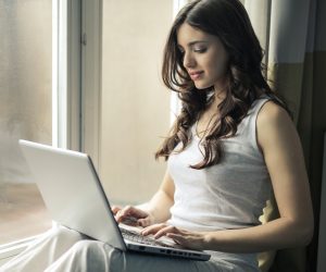 Woman sitting by a window with her laptop.