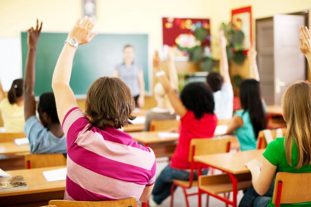 Group of teenagers sitting in the classroom with raised hands. - A ...